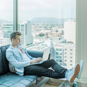A young man working on a laptop in a penthouse overlooking the city